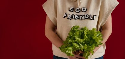 Woman in an eco-friendly hoodie holding fresh lettuce against a red background.
