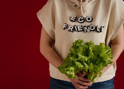 Woman in an eco-friendly hoodie holding fresh lettuce against a red background.